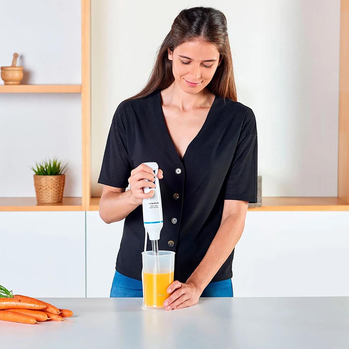 Kvinna använder stavmixerset Taurus Robot 750 Easy för att mixa en orange dryck i köket