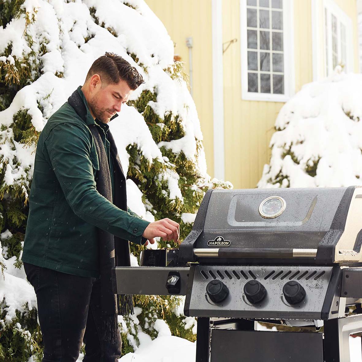 Man som grillar på en gasolgrill utomhus i snöigt vinterlandskap