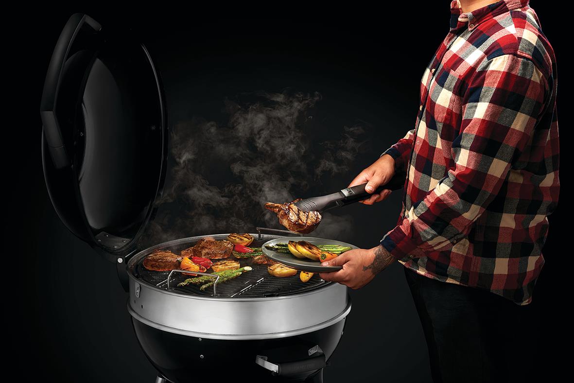 Person som grillar kött och grönsaker på en svart kolgrill Napoleon Pro 22K-L-3