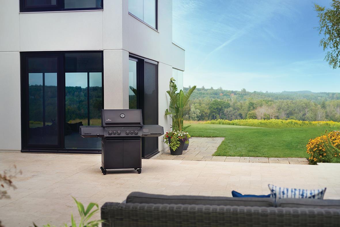 Gasolgrill Napoleon Prestige 500 Connected 6 Brännare Phantom utomhus på terrass med modern villa och grön trädgård i bakgrunden