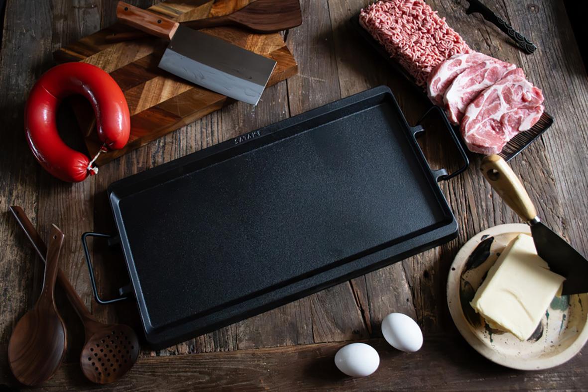 Stekbord Satake gjutjärn på träbord med köksredskap och ingredienser