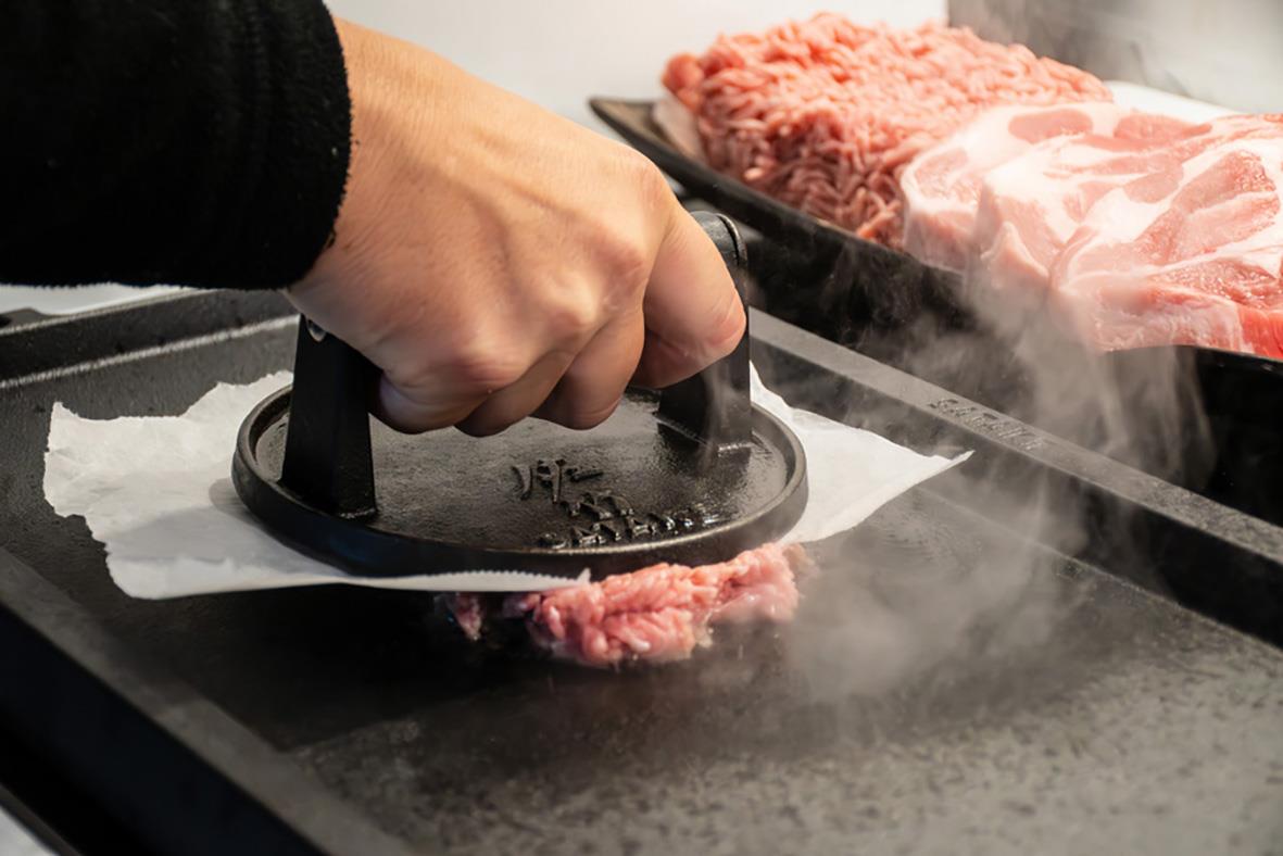 Person steker kött på en gjutjärnssatsake med en tryckpress