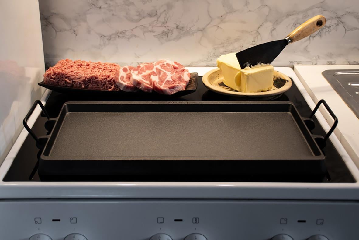 Stekbord Satake gjutjärn med kött, smör och stekspade på en spishäll