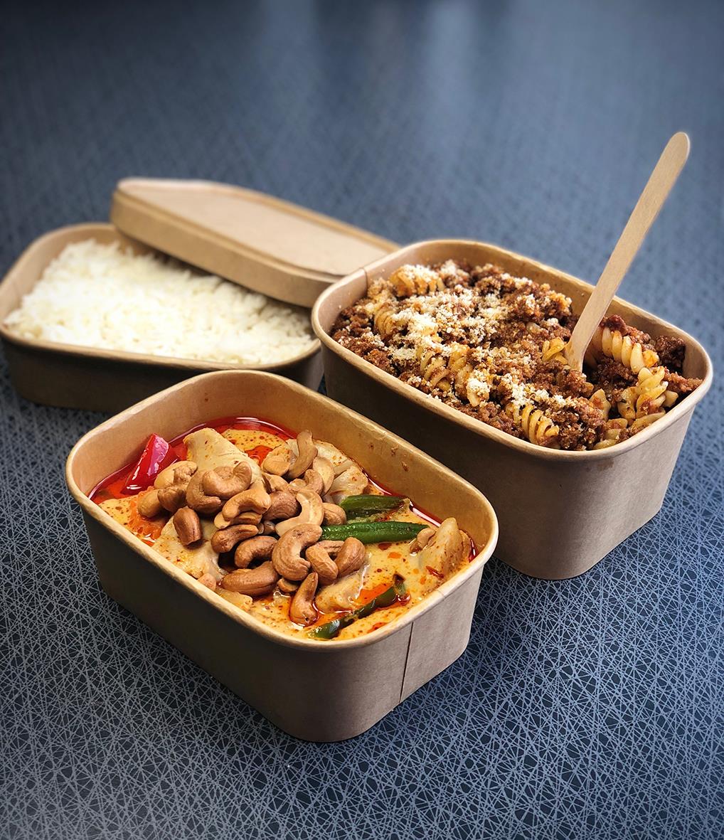 Två pappersformar med mat, en med ris och en med köttfärssås, på en blå yta