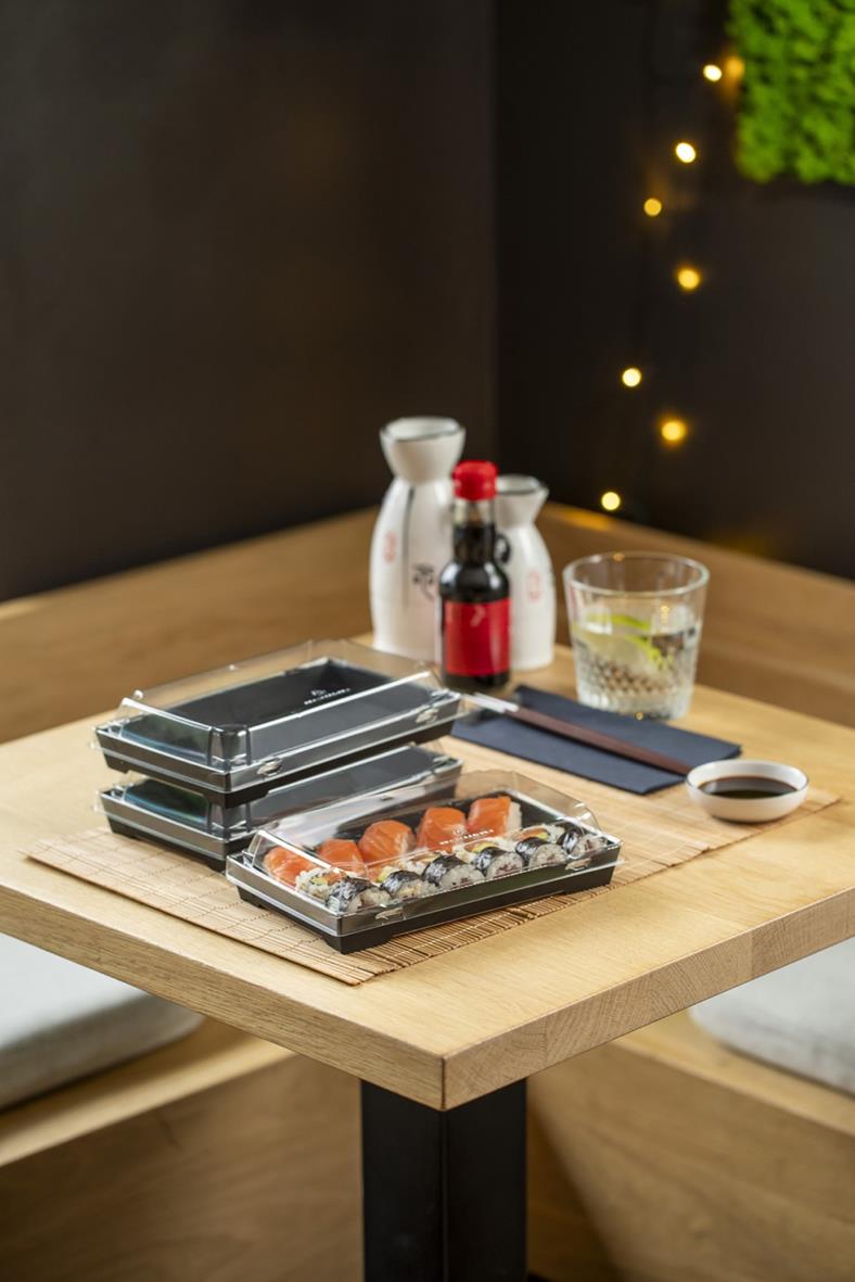 Svart pappersform Tray2Go Sushi på ett bord med soja, wasabi och dryck i bakgrunden