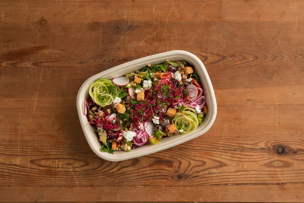 En oval pappersform fylld med sallad på ett träbord