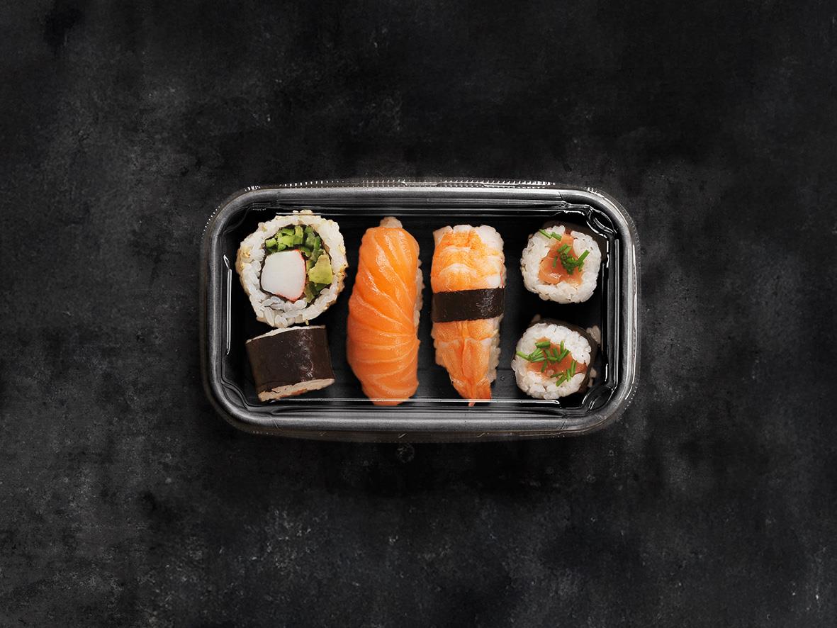Sushi i svart plastlåda med lax, räk- och grönsaksrullar