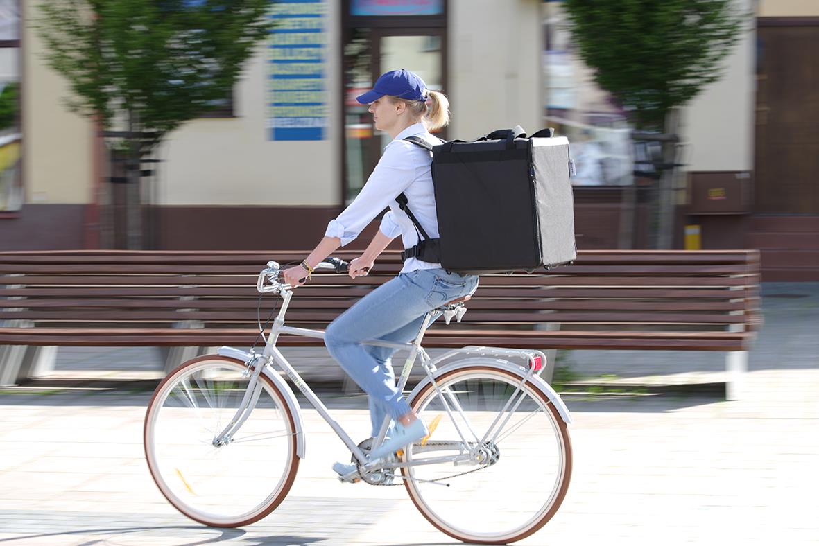Kvinna cyklar med svart termoväska/ryggsäck Hendi på ryggen i stadsmiljö