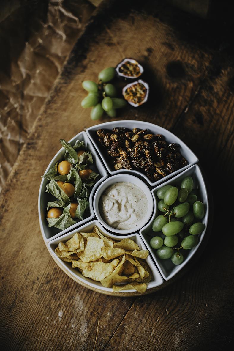 Snurrbricka med olika tilltugg som druvor, chips, frukt, nötter och dipp på en träbänk