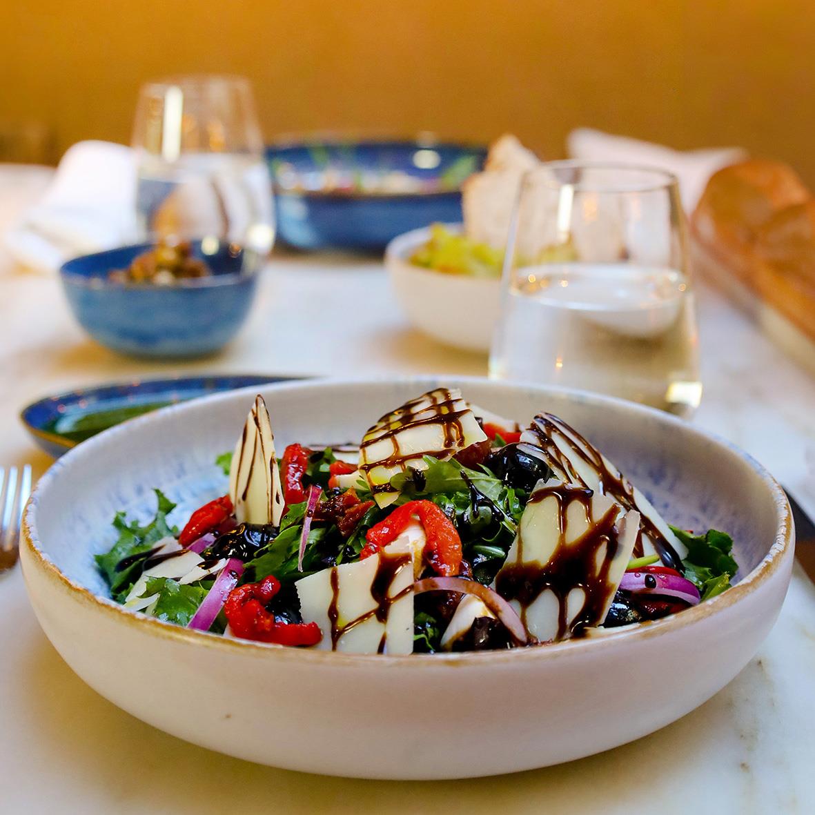 Blå skål med sallad och dressing på ett bord med andra skålar och drycker