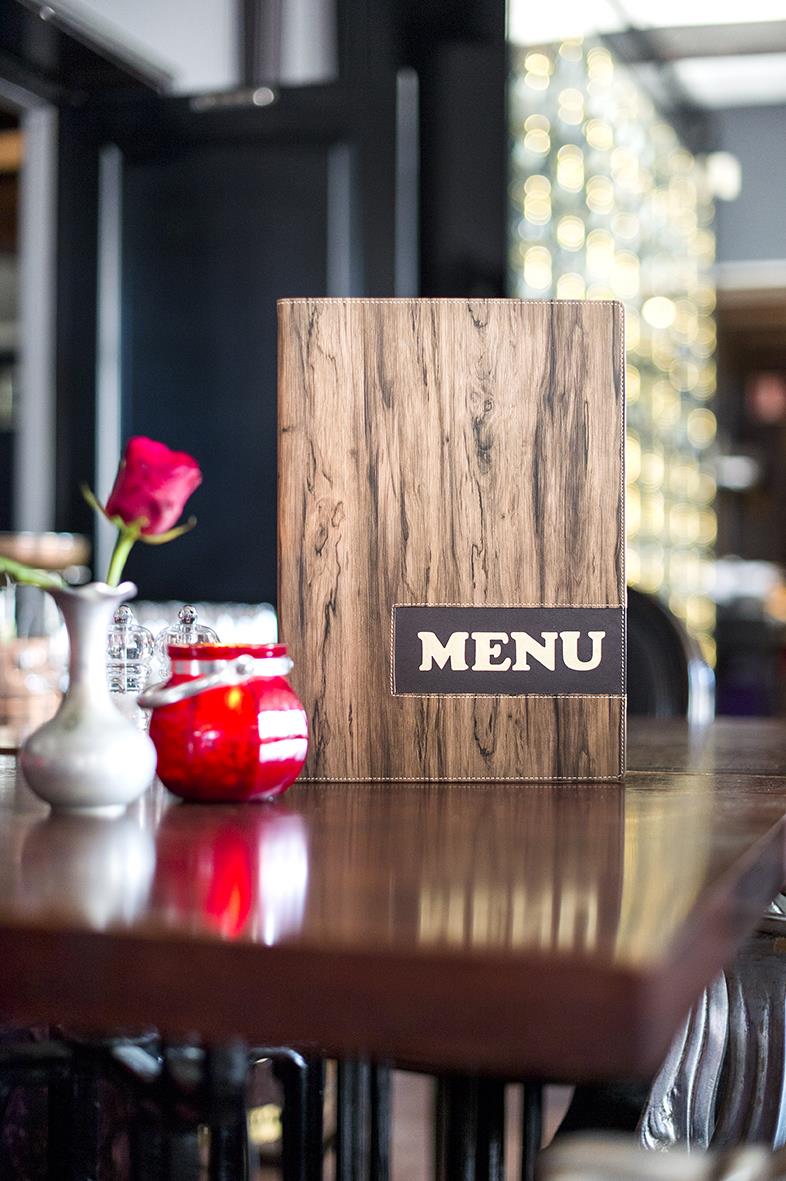 Menypärm i brunt trädesign med svart etikett och vitt text MENU på bord i restaurangmiljö