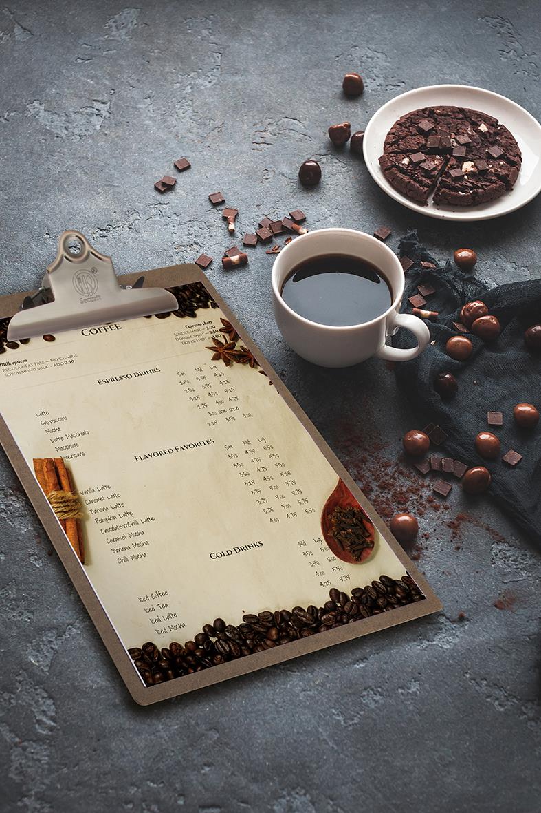 Menynhållare Securit med klämma i brunt, placerad på ett bord med kaffe, choklad och kakor