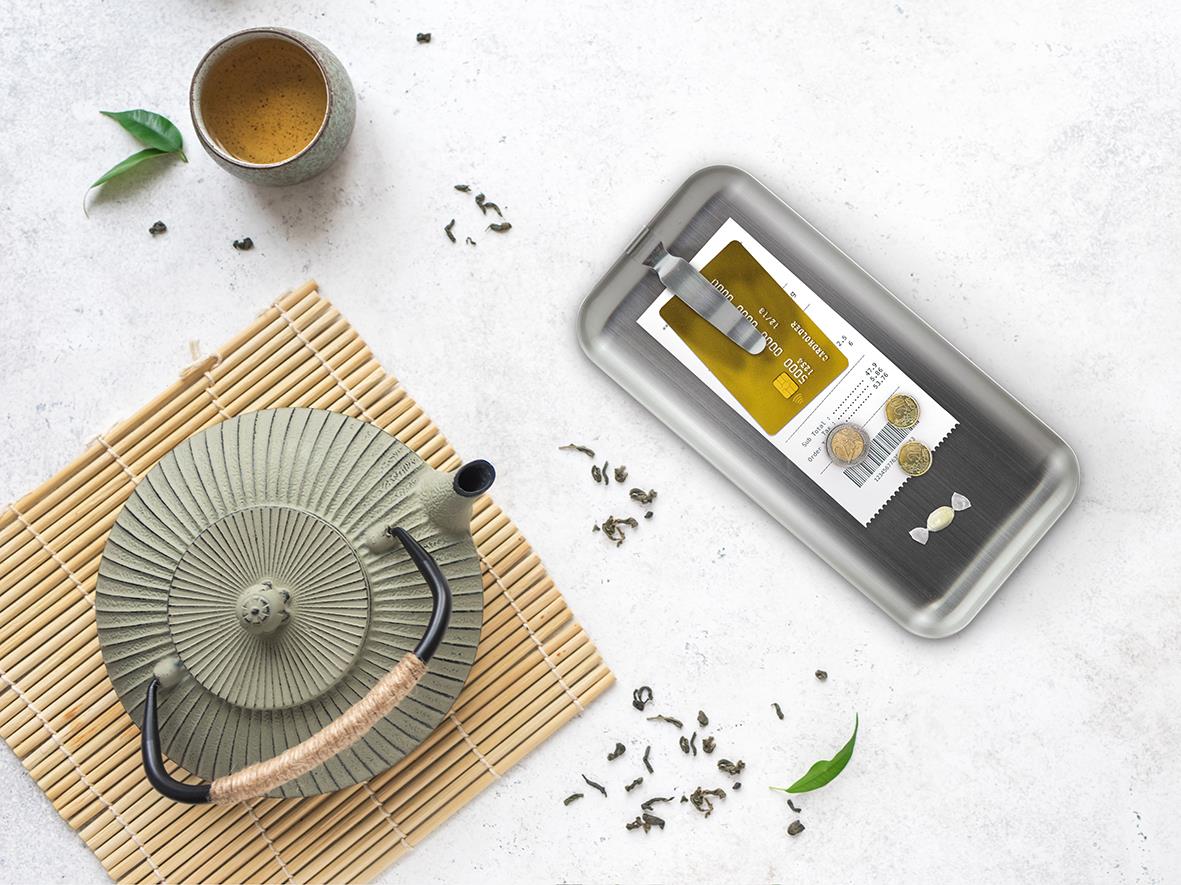 Notbricka i stål med klämma, mått 28,5x9cm, på vit bakgrund med te, växtblad och teblad