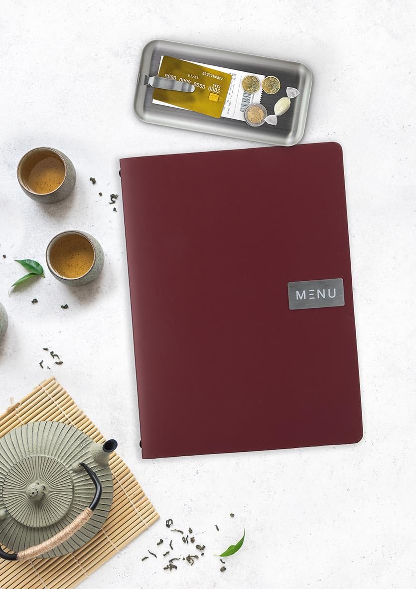 Röd notbricka med klämma, samt en metallask med mynt, ett tefat med te och två koppar, och ett te-set på en vit bakgrund