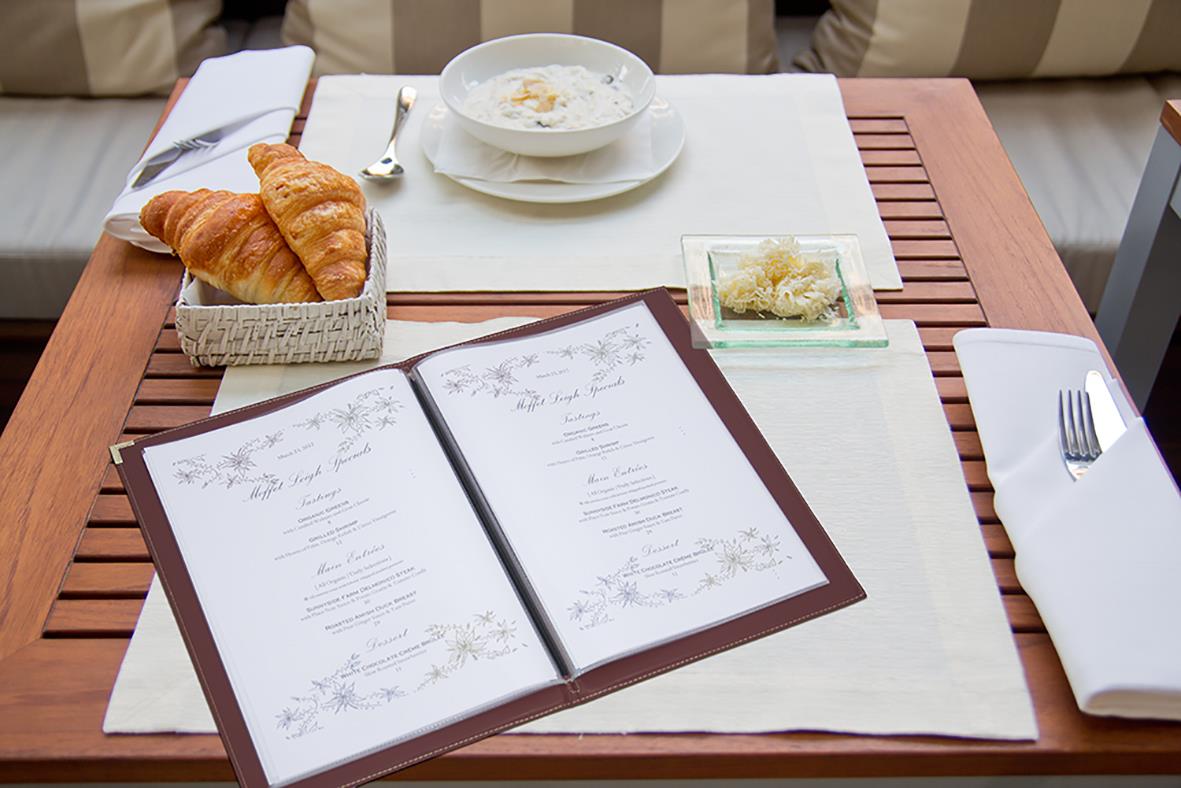 Meny med plastficka Securit till A4, ett glas vatten, croissanter och bestick på ett bord