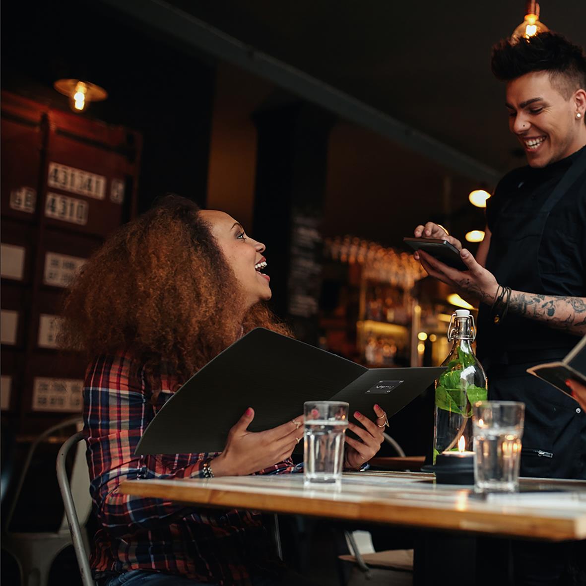 Kvinna och man i restaurang, kvinna håller menypärm, man tar beställning, mörk bakgrund, varm belysning