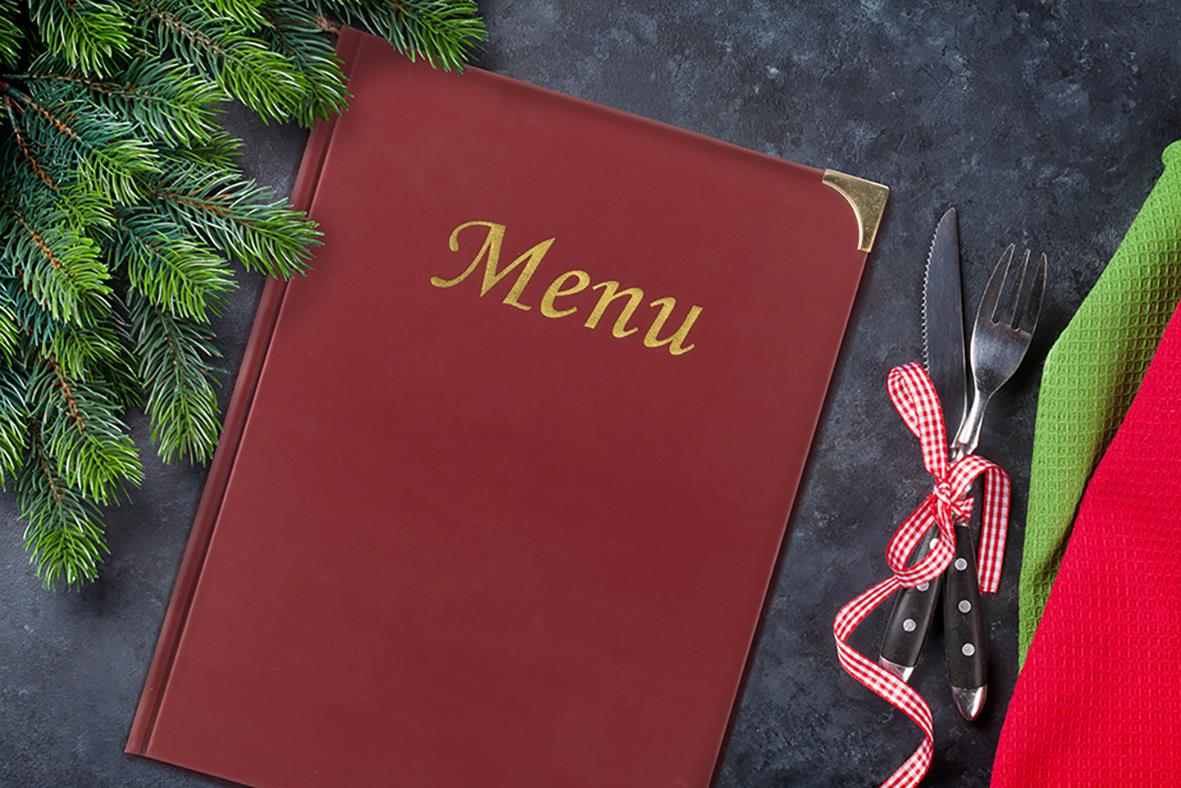 Vinröd menypärm med gul text Meny på A4, placerad på mörk bakgrund med grönt granris och bestick med rödvit band