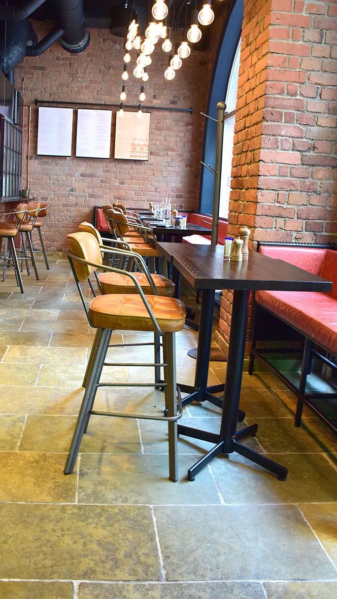 Inomhusbild av ett svart bord med fliptop funktion, omgiven av stolar och barstolar i ett modernt café eller restaurang med tegelväggar och takbelysning