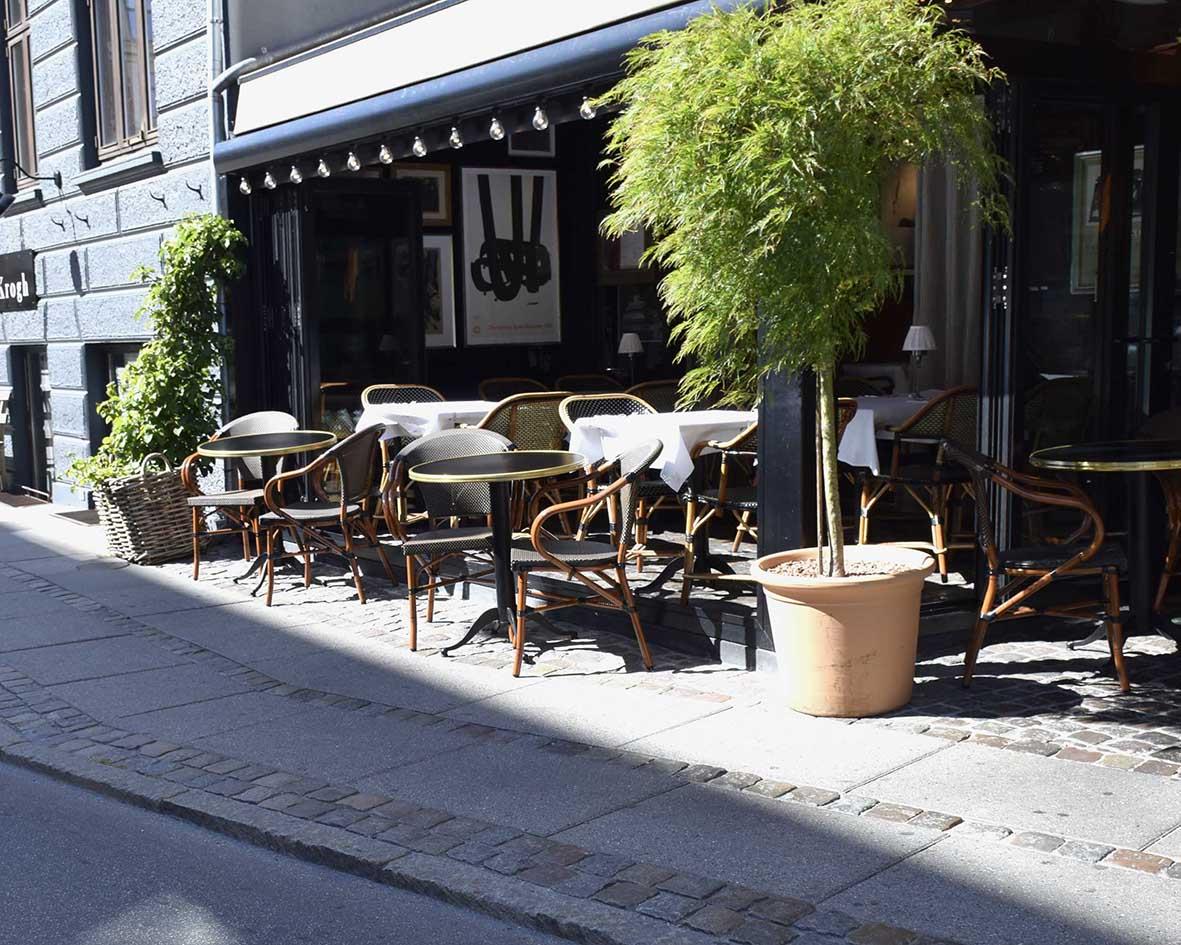 Uteservering med vintage träbord och vita stolar utomhus på trottoaren