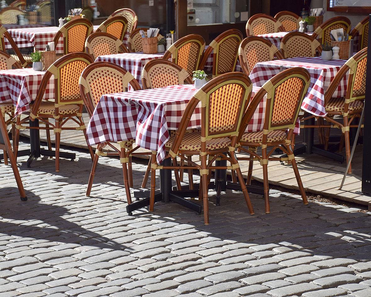 Uteplats med flera bord och stolar med rödvit rutiga dukar på stenbelagd yta