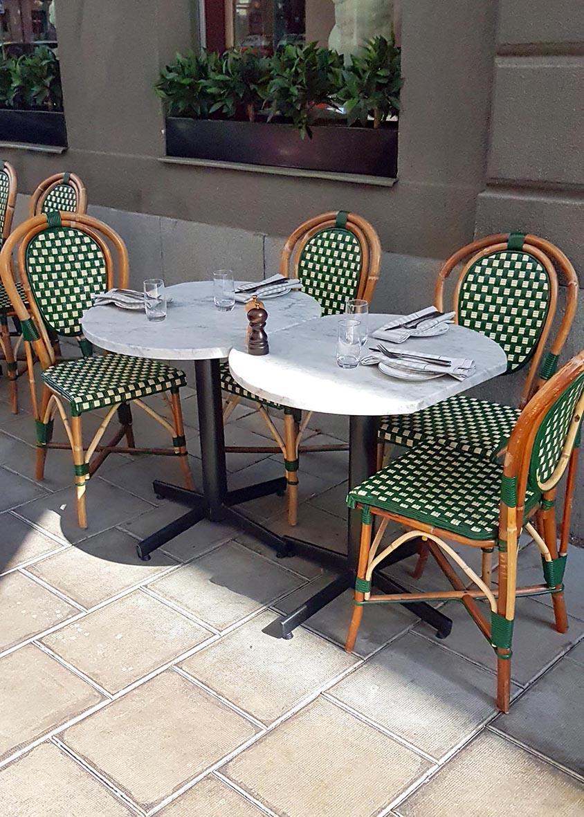 Bord med två delar, en rund och en oval, med gröna och vita stolar runt, utomhus på stenbelagd terrass