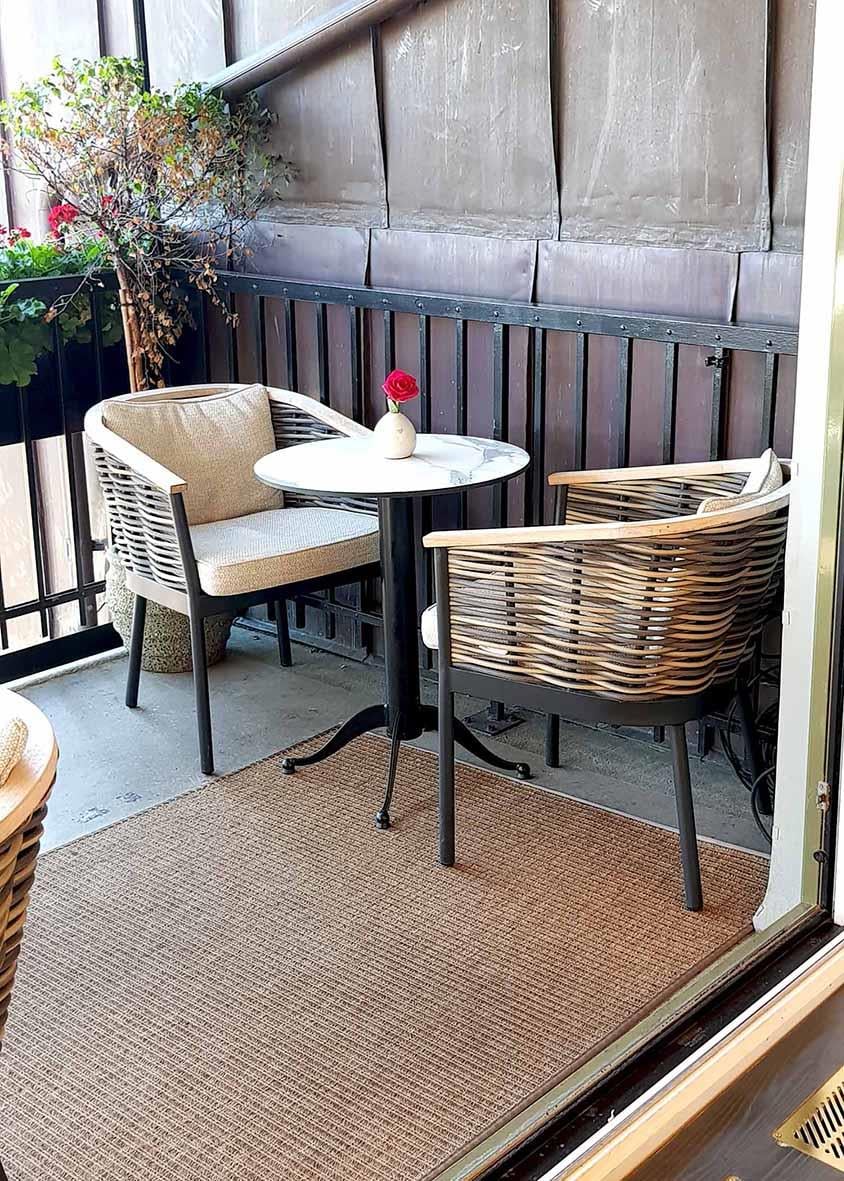 Bordsskiva Stable Table i brunt trä med två stolar på liten balkong, utomhusmiljö