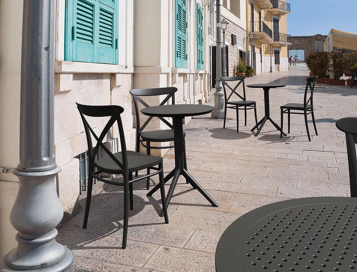 Svart stapelbar plaststol och bord utomhus på gata med byggnader och fönster i bakgrunden