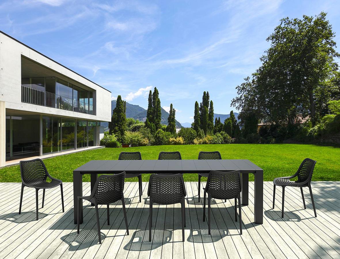 Svart stapelbar stol utomhus vid modern villa med grön trädgård och blå himmel