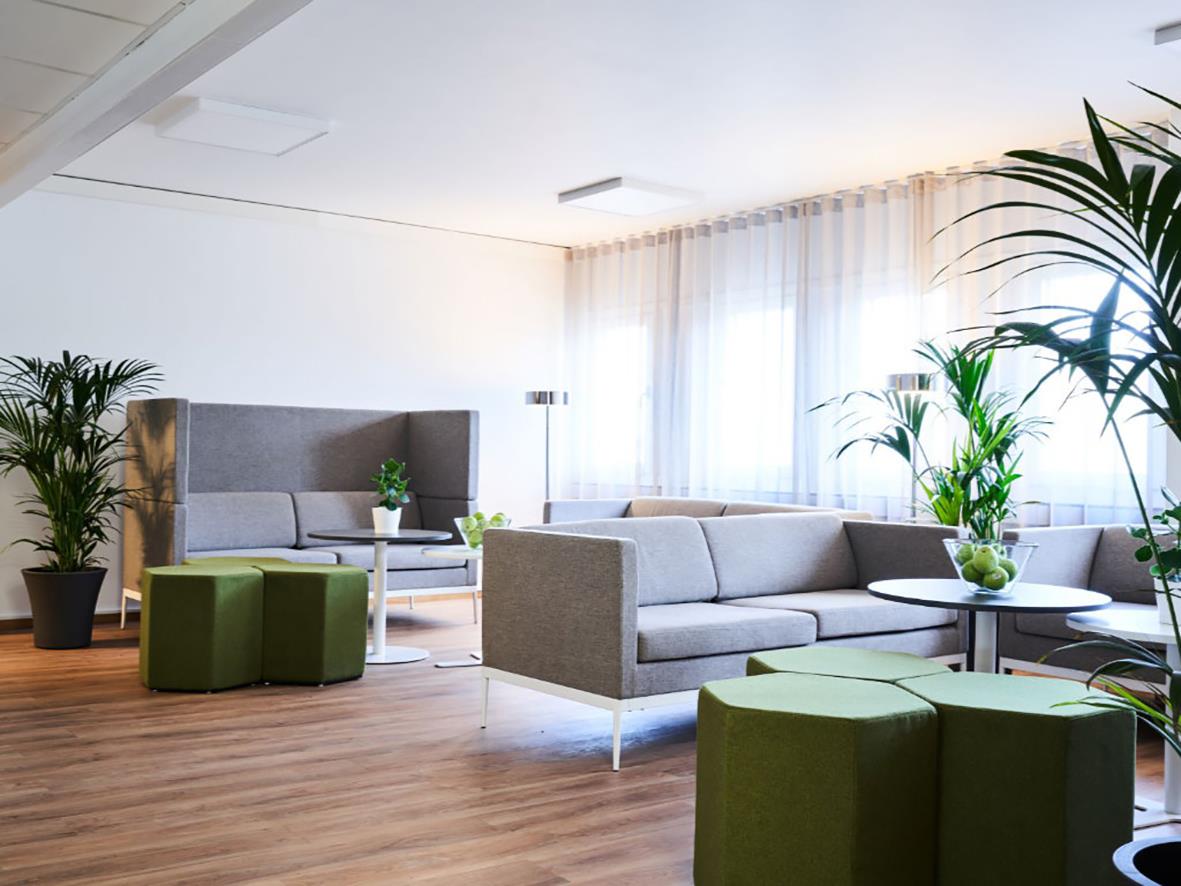 Soffa Lotus Bergamo 3-sits låg rygg i grått i ett ljust vardagsrum med gröna växter och stora fönster