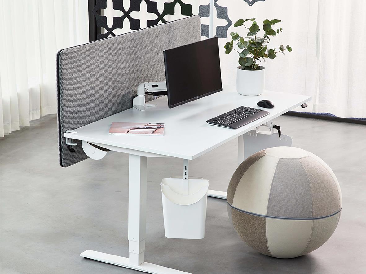 Kontorsbord med skärmvägg, dator, växt och sittpuff i ett modernt arbetsutrymme