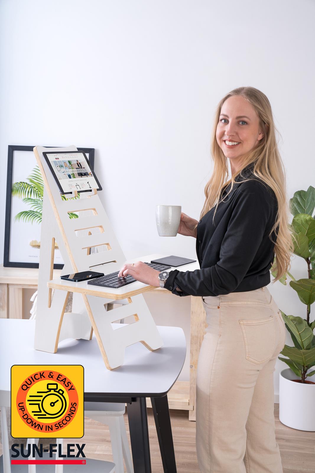 Kvinna använder portabelt höj- och sänkbart ståbord Sun-Flex Easydesk Rise i vitt, med laptop och kaffekopp i ett kontorsmiljö
