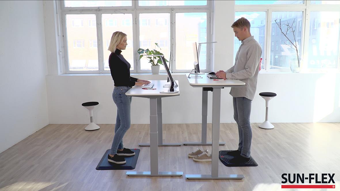 Två personer använder ett höj- och sänkbart skrivbord Sun-Flex i ett ljust kontor