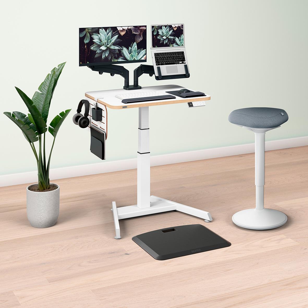 Arbetsstation med två bildskärmar, laptop, hörlurar, växt, stol och våg på ett ljust golv