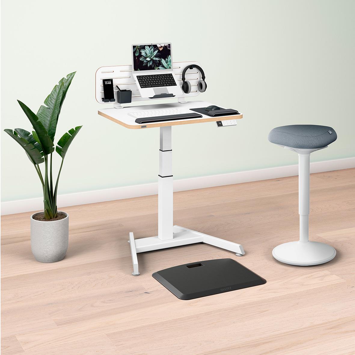 Arbetsstation med Leitz Ergo Compact Pro-laptop, växt, skrivbordstillbehör och en rund stol i ett minimalistiskt rum