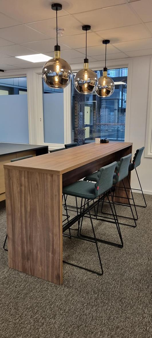 Barbord av trä med tre gröna stolar under tre moderna glaskuporhänglampor i ett inomhusmiljö