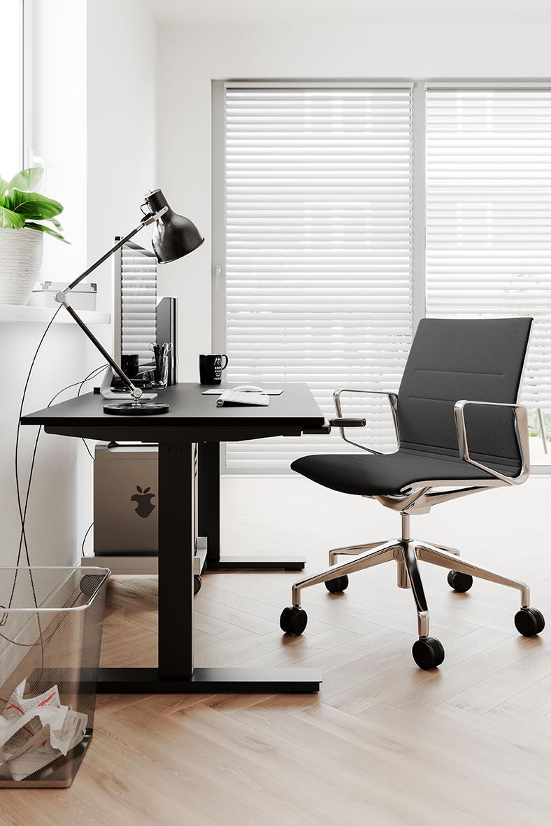 Konferensstol i mörkgrå placerad vid skrivbord med dator och skrivbordslampa i ett ljust kontorsrum