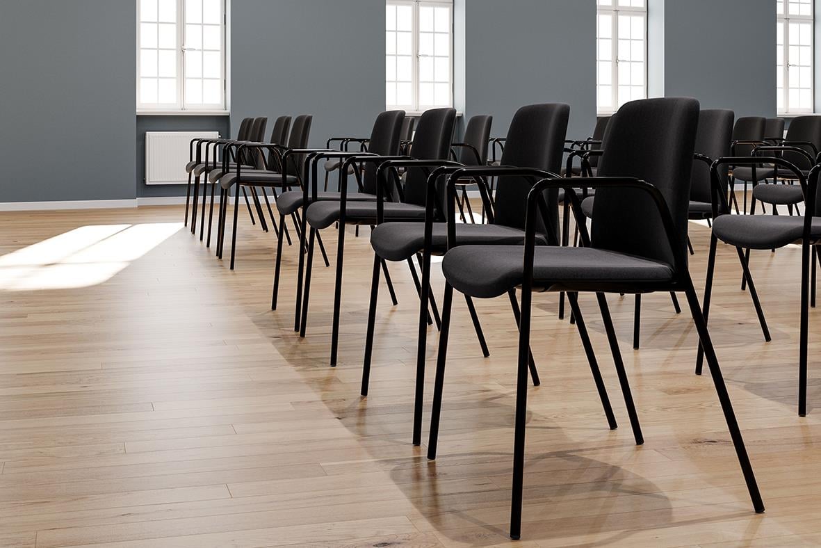 Svarta tygklädda stolar i rad i ett tomt rum med stora fönster och trägolv