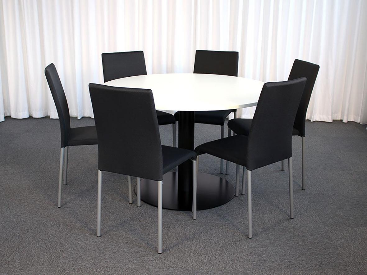 Rund bord med sex svarta staplingsbara stolar i mörkgrått tyg framför en vit gardin