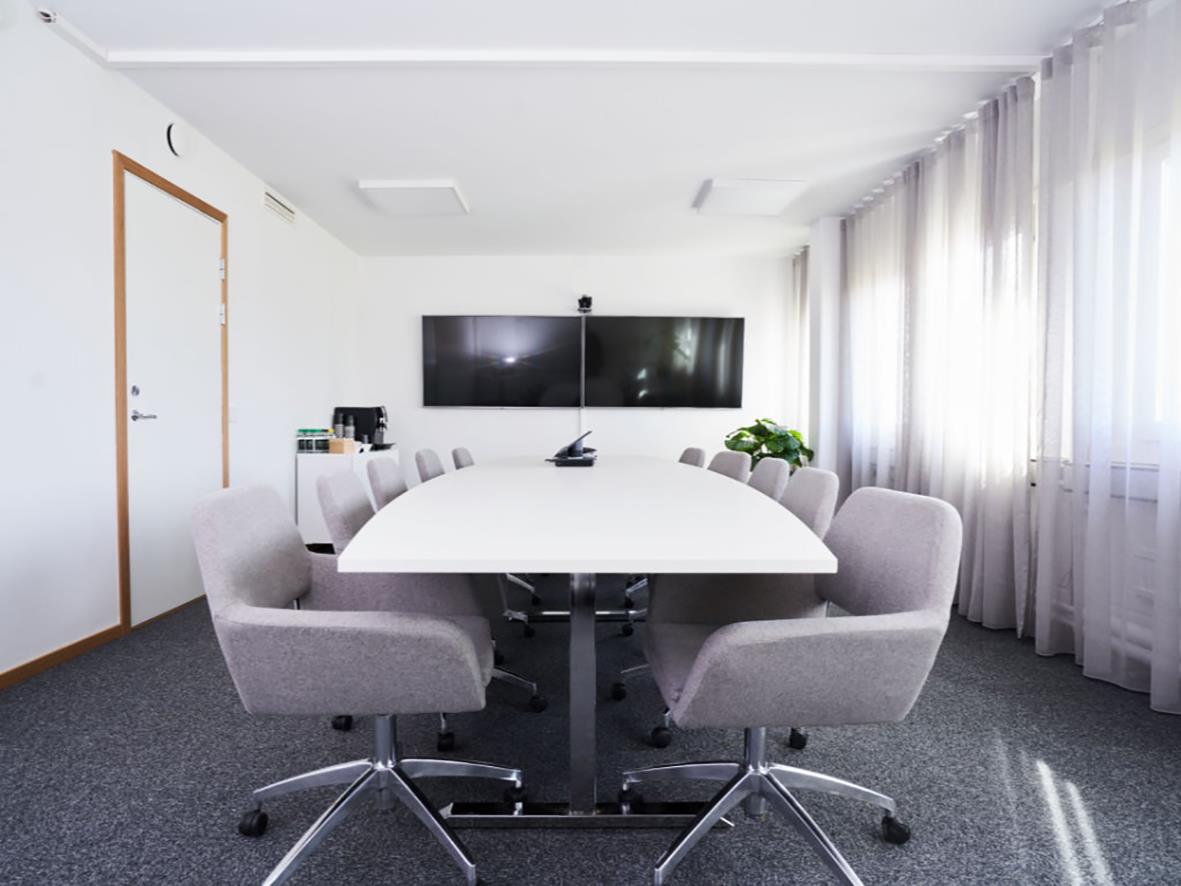 Konferensbord i vitlaminat i ett mötesrum med åtta stolar och en stor skärm på väggen