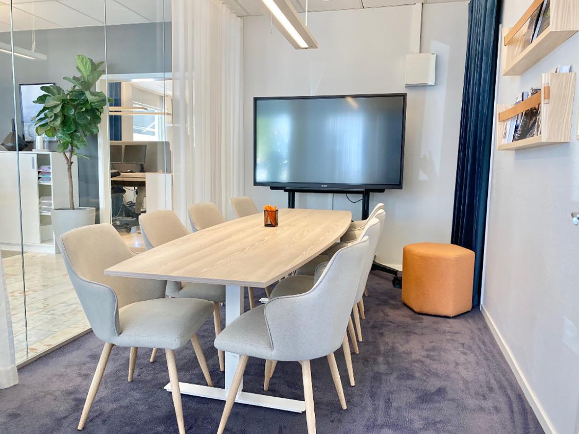 Konferensbord i ljus ek med åtta stolar i ett mötesrum med TV och växter