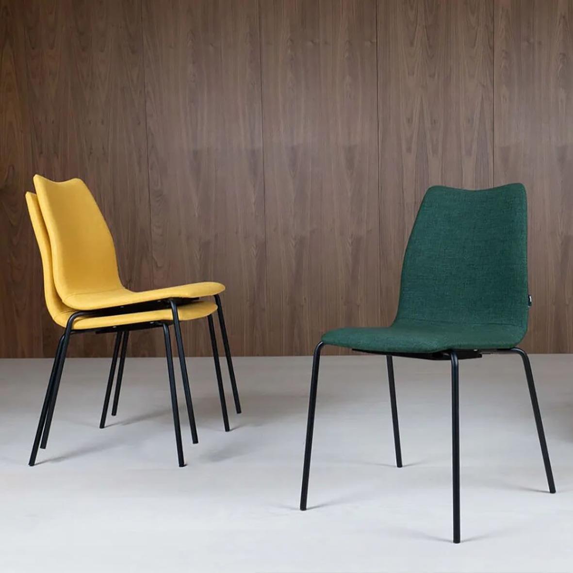Två moderna stolar, en gul och en grön, står på en vit golv mot en trävägg