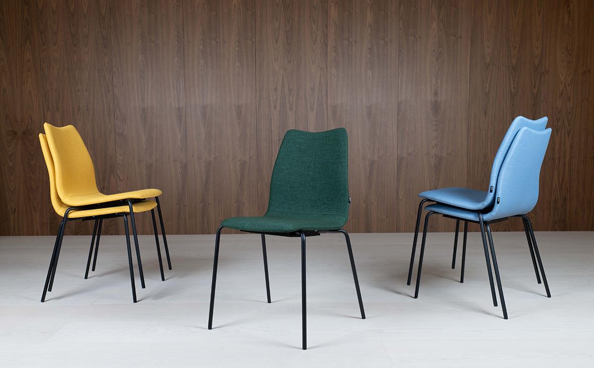 Tre färgglada stolar i rad framför en trävägg, gul, grön och blå