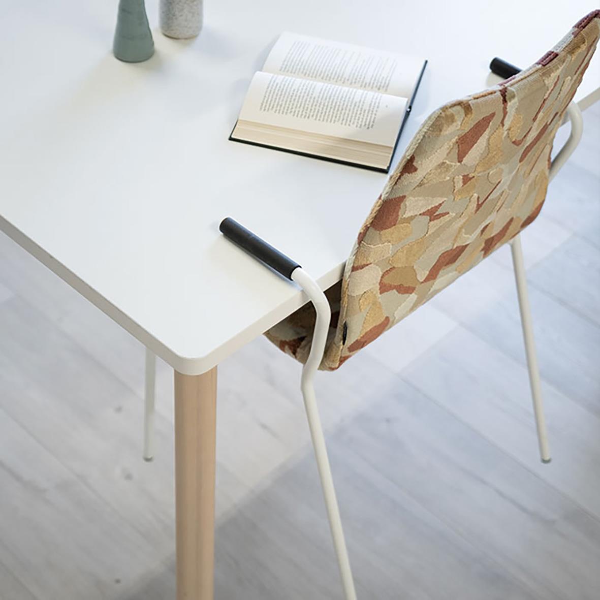 Vitt skrivbord med öppen bok och en stol med mönstrad sits