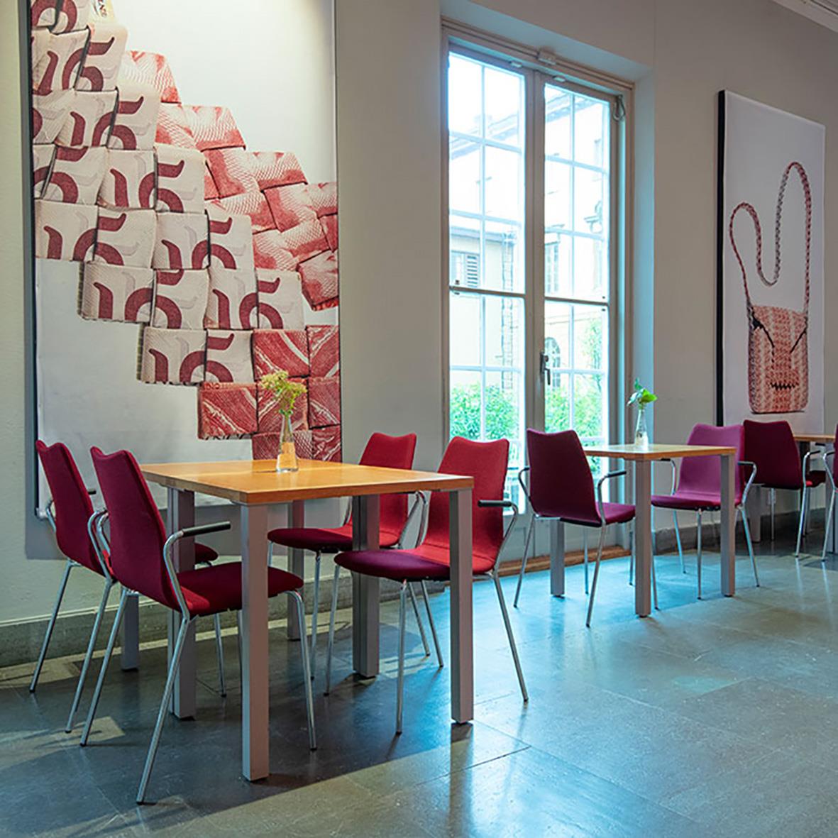 Möblerad café eller lounge med röda och lila stolar, stora fönster och konst på väggarna
