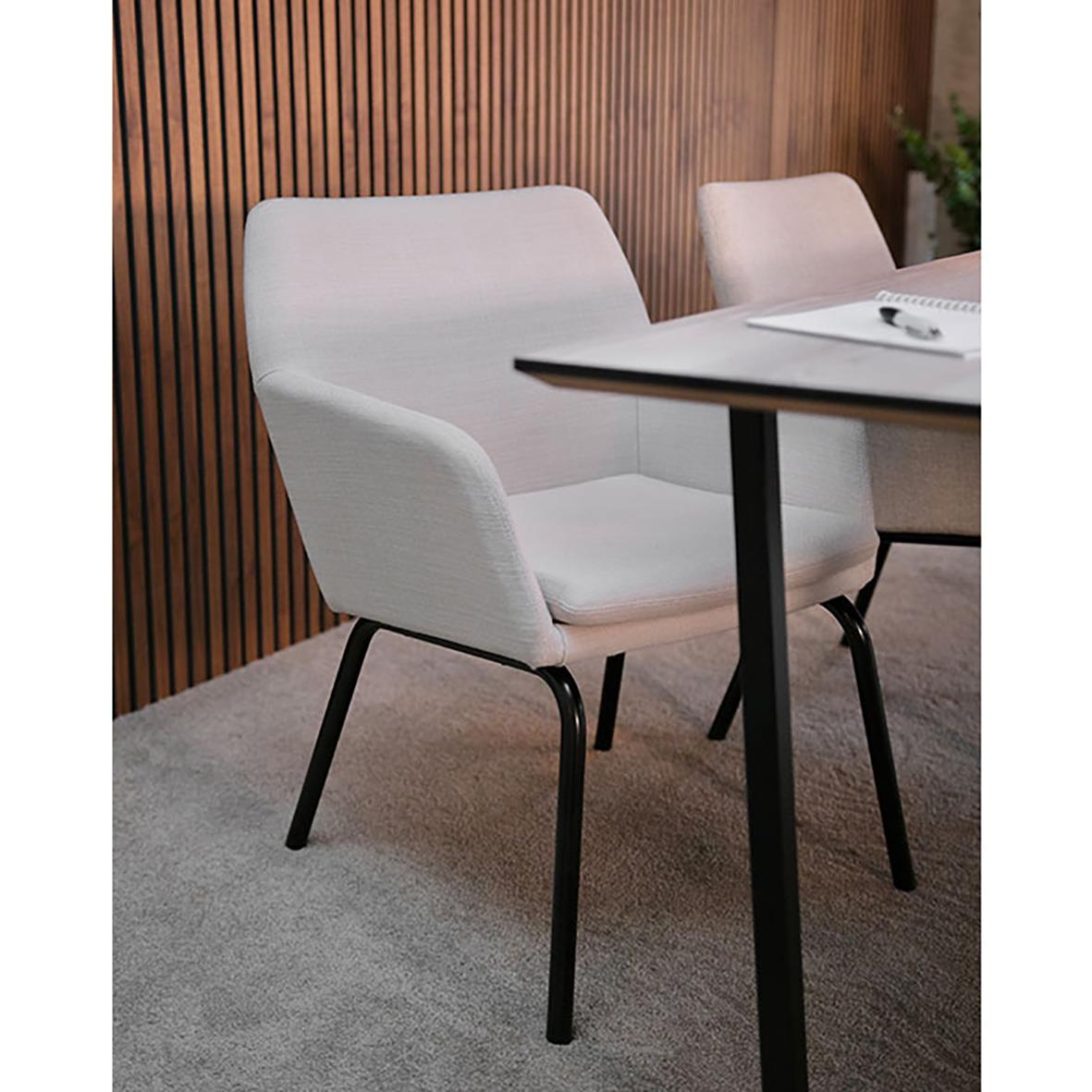 Karmstol ioff Solo helklädd i beige och svart framför ett bord med trävägg i bakgrunden