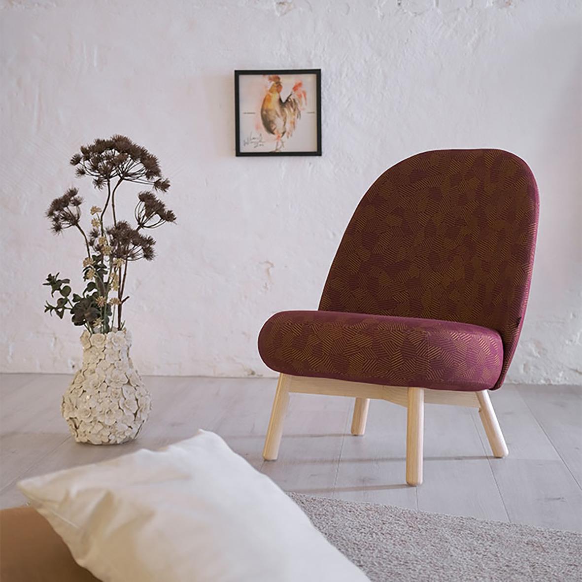 Mörkröd fåtölj med ljus träram framför vit vägg med konst av höna och en vas med torkade blommor