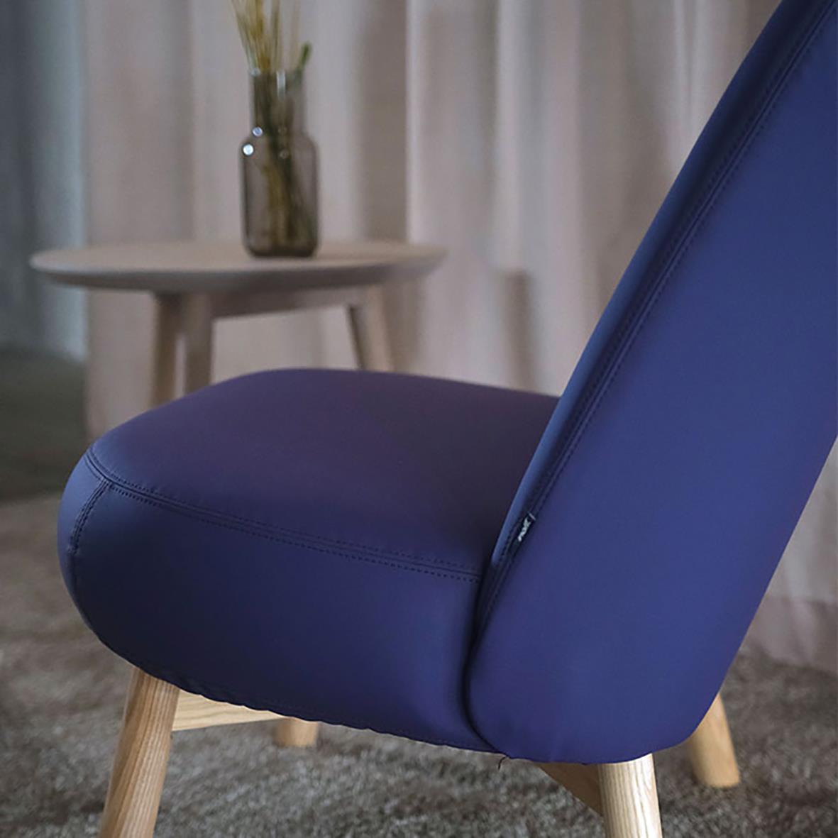 Blå stol med träben i ett vardagsrum med gardiner och ett bord med växt i bakgrunden