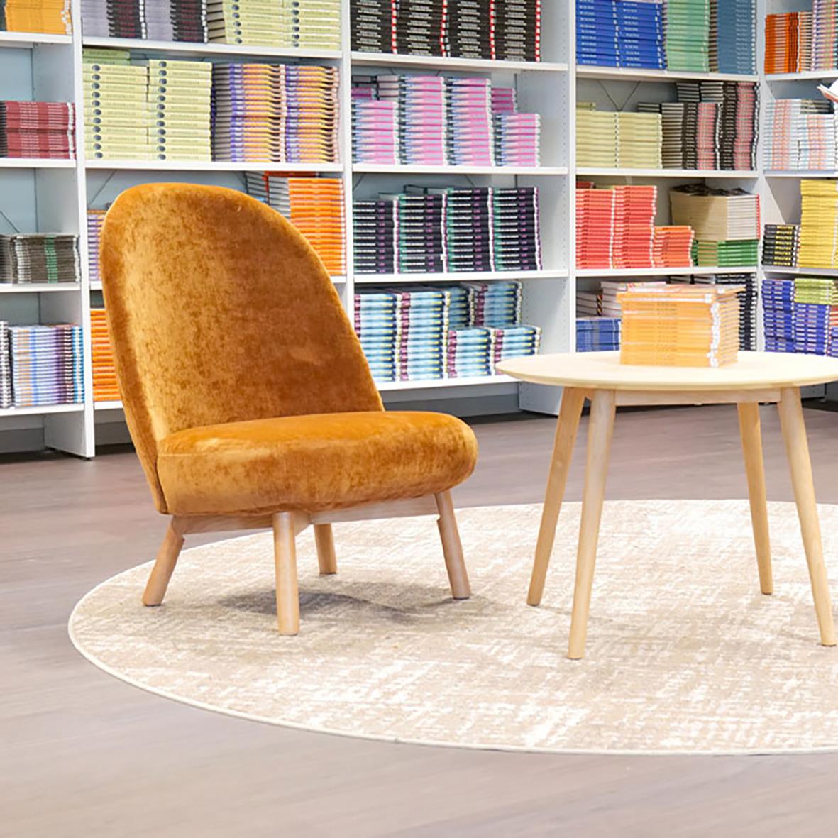 Mörk orange fåtölj och ett runt bord i ett bibliotek med hyllor fyllda med böcker