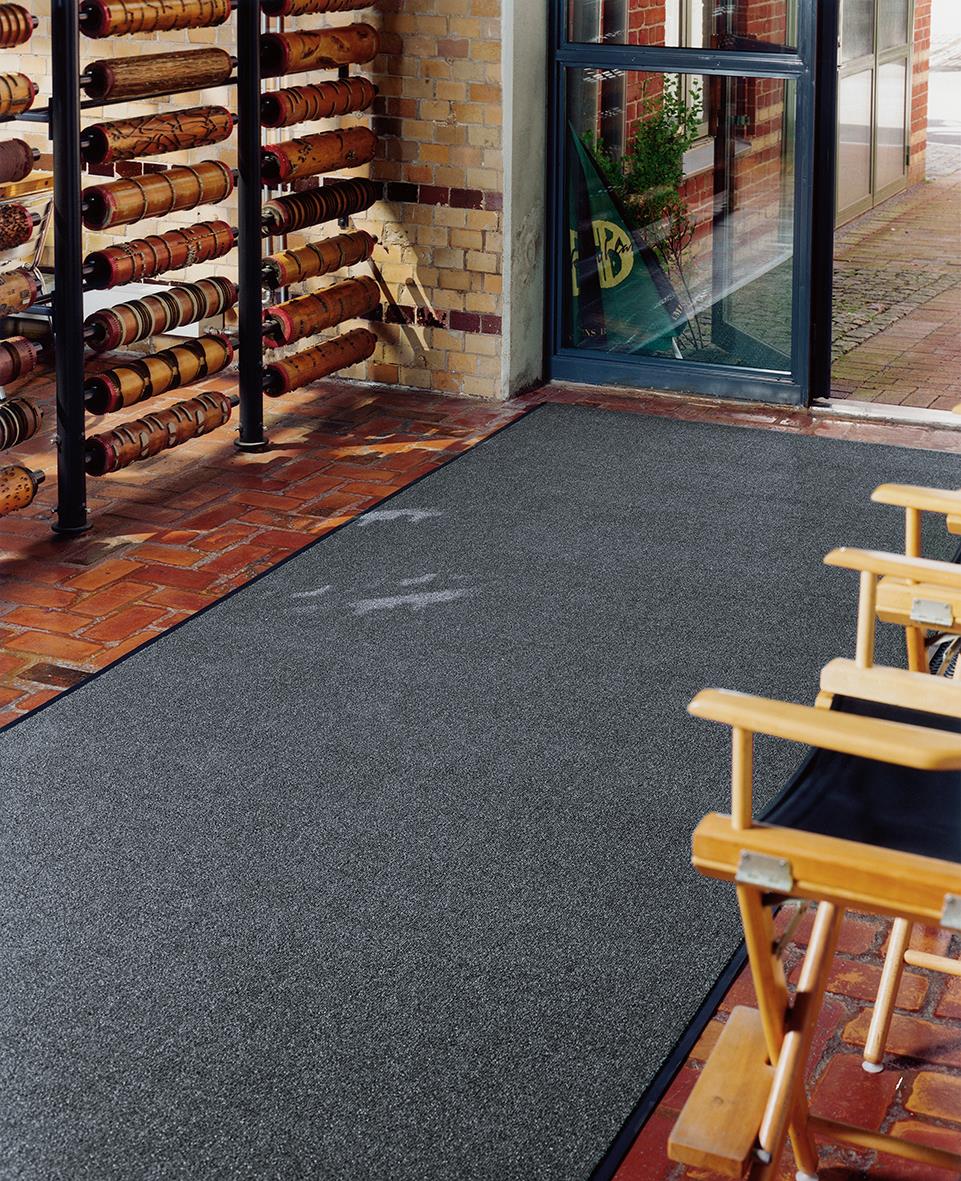 Kombinationsmatta 90x150cm på uteplats med stolar och glasdörr, vägg med brickor och rullstolsställning i bakgrunden