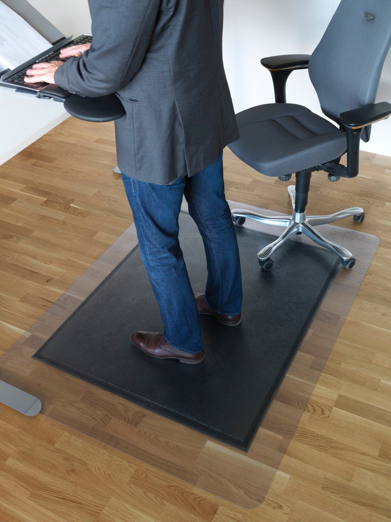 Person står på en svart arbetsplatsmatta framför ett skrivbord och en kontorsstol på ett trägolv